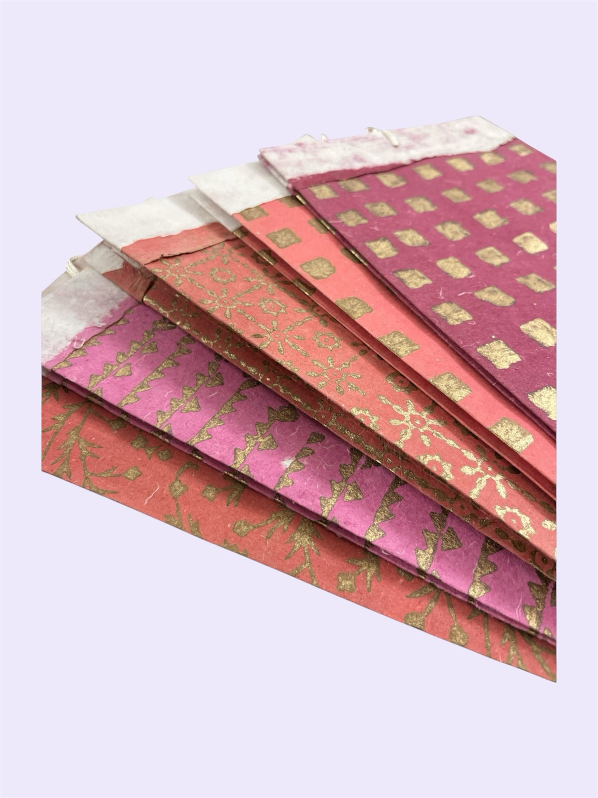 Bombay Paperie handmade paper gift bags in red and pink with gold-foiled patterns and rustic deckled-edge tops.