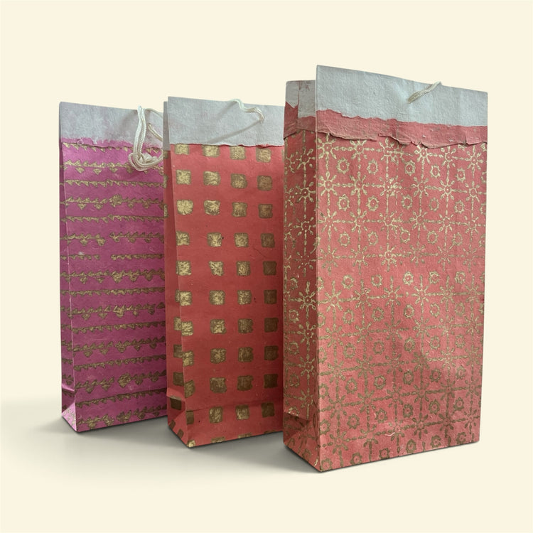 Bombay Paperie handmade paper gift bags in red and pink with gold-foiled patterns and rustic deckled-edge tops.