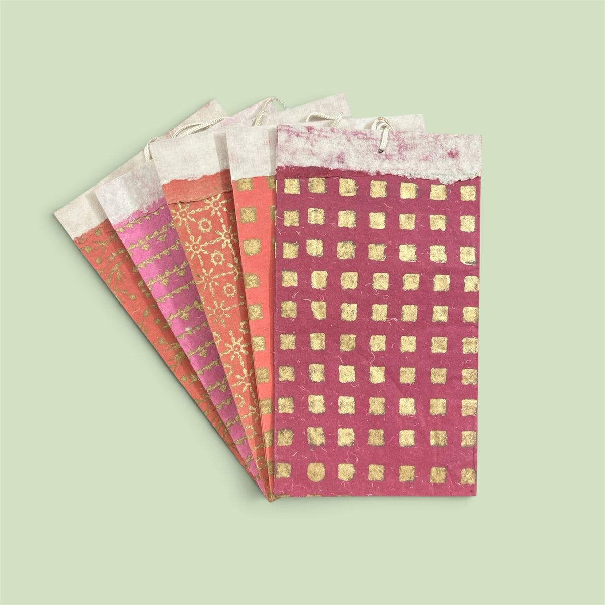 Bombay Paperie handmade paper gift bags in red and pink with gold-foiled geometric patterns and rope handles.
